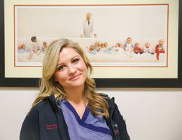 female nurse poses for photo in front of picture of Dr. Bailey and children he helped