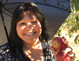 Regina Juarez smiles while holding apples picked from an apple orchard