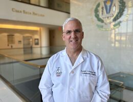 Dr. Randall Fortuna wearing white coat in hallway smiling
