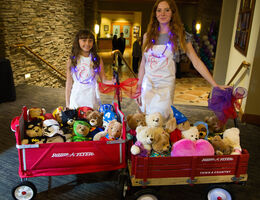 two young girls standing with red wagons full of teddybears 
