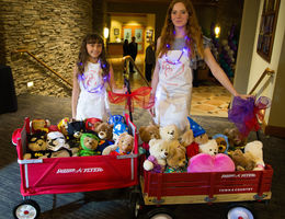 two young girls standing with red wagons full of teddybears 