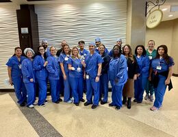 A large group of people in medical scrubs posing together in a hospital lobby.