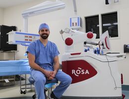 Doctor in blue scrubs sitting in front of a Rosa robot 