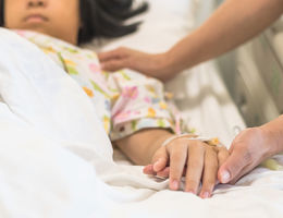 Nursing caretaker concept with kid patient sleeping in bed with family caregiver hand support in blur medical hospital background (focus on hand)