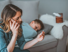 worried mother taking temperature of her little son who is lying in bed with fever