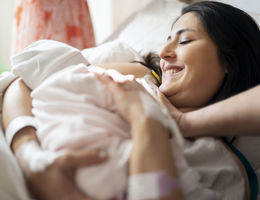 Mother breastfeeding newborn baby in hospital ward, first breastfeeding