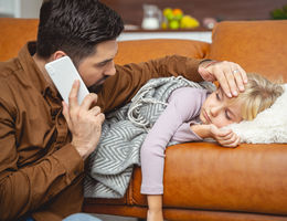 Caring father calling doctor and touching daughter forehead