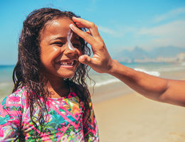 Little surfer girl preparing for surf with suntan lotion on a face