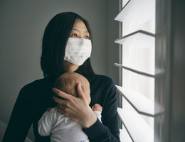 A mother wearing mask and holding baby in home isolation from infectious disease