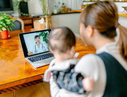 A mother with her baby is video calling a doctor on a laptop from home