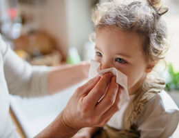 Unrecognizable father with small sick toddler daughter indoors at home, blowing nose.