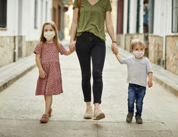 Mother with daughter and son, holding hands walking on the street, wearing home made face mask for coronavirus pandemic.