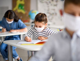 Small children with face mask back at school after covid-19 quarantine and lockdown, writing.