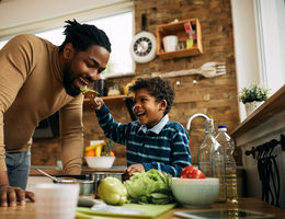 Happy African American boy having fun while feeding his father in the kitchen.