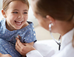 young female doctor listening to heart of young smiling girl