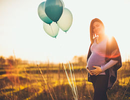 Pregnant woman standing in the middle of a field with balloons.