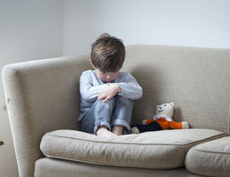 Little boy suffering from child abuse curled up on the sofa with his teddy.