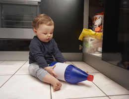 child sitting on the floor holding household chemical bottle from under the sink cabinetry