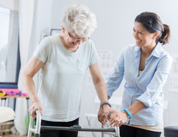 Older woman standing with walker with help from another woman