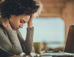 women rubbing her head while sitting in front of a computer screen