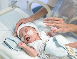 Premature baby in an incubator with oxygen and unrecognizable mom caressing baby trying to calm him down