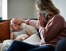 hot of a mother wearing a surgical mask making a phone call while aiding to her sick young son at home