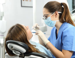 Female dentist cleans the teeth of a female patient in a dental office.