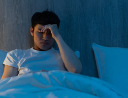 Young male sitting up in bed pinching his head as if in pain