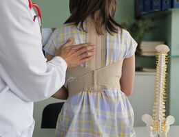 Doctor adjusts spine brace on young patient in a clinical setting, focusing on health and wellness