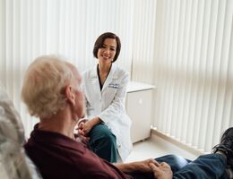Asian female doctor sitting in a doctor's office with a male, white-haired man