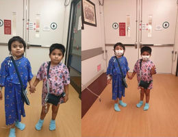 two young boys standing in hospital gowns holding hands