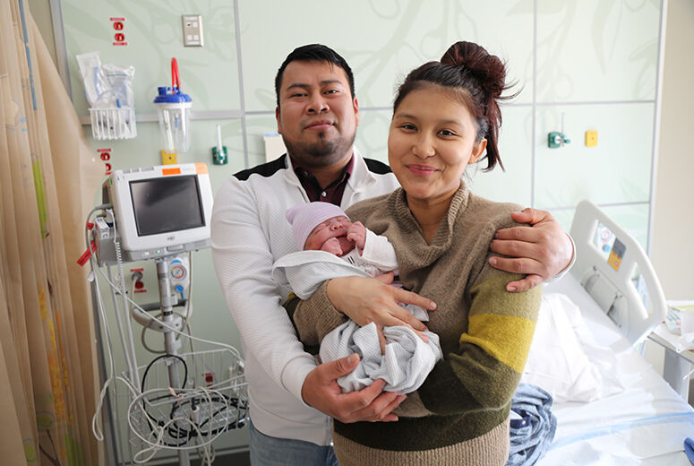 mother holding baby with dad standing behind arms wrapped around mother and baby