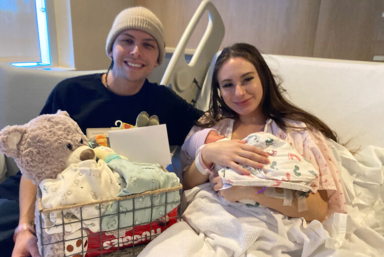 mother in hospital bed holding baby and smiling, dad sitting beside smiling
