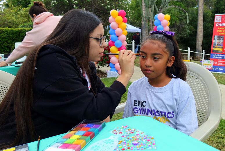 A volunteer paints a small design on a child’s face at a craft table during the event.