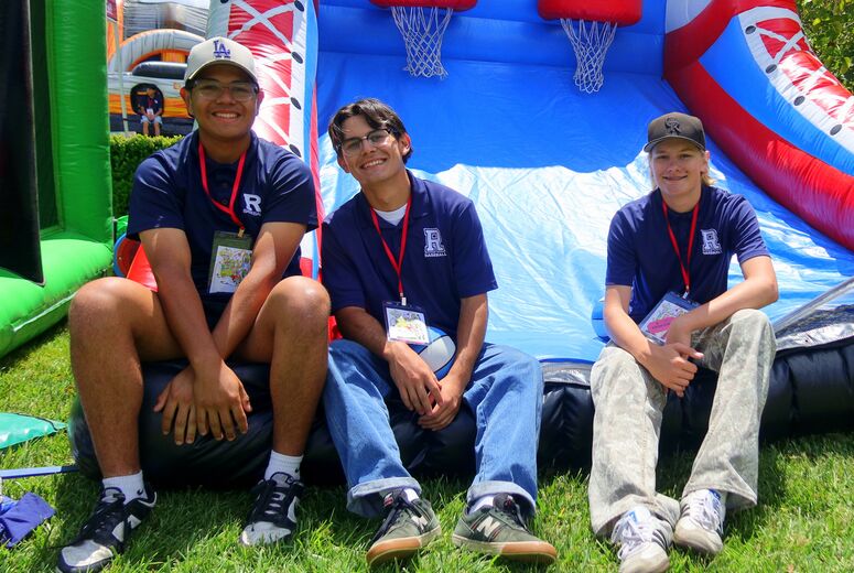 Three volunteers sit together in front of an inflatable activity during the event.