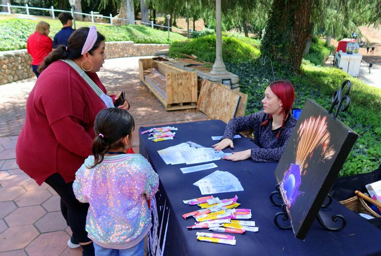 Event staff assist guests at a table with wristbands and informational materials.