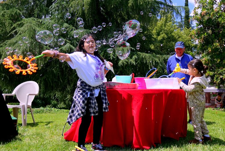 Children and adults play with bubble wands near a table filled with bubble supplies.
