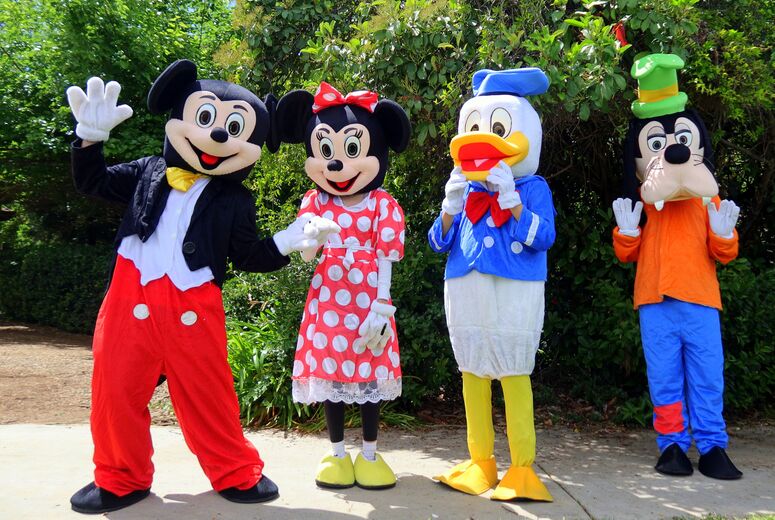 Costumed character performers stand together outdoors, posing for photos with guests.