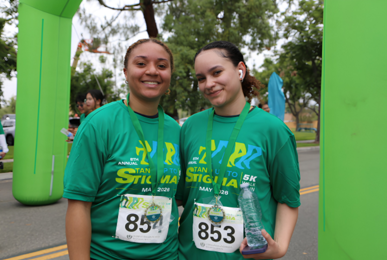 Two participants wearing medals stand together at a 5K event finish area.