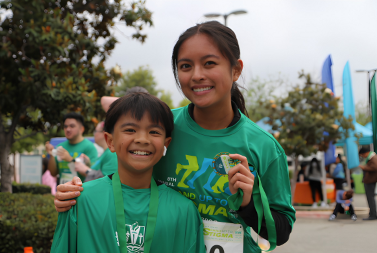 Participant and child wearing medals pose together at a 5K event.