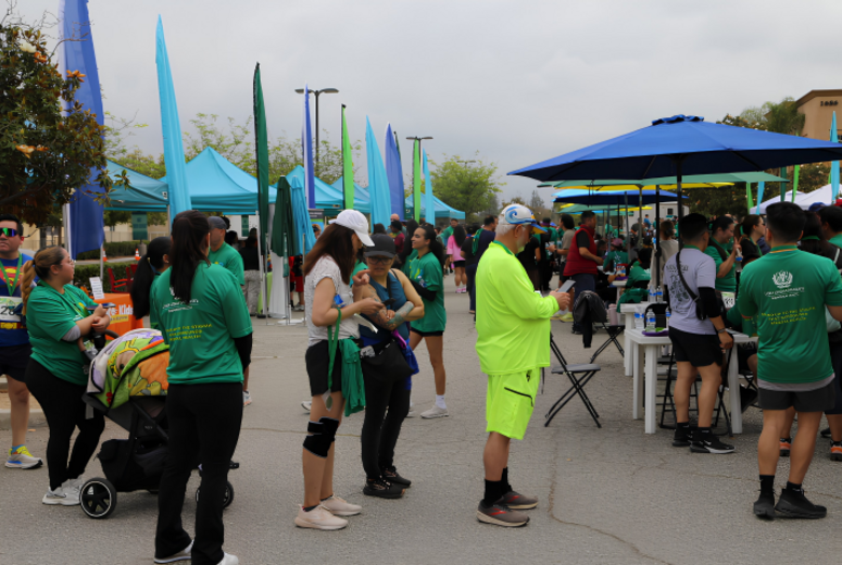 Crowd of participants in green shirts gather near tents and tables at a 5K event.