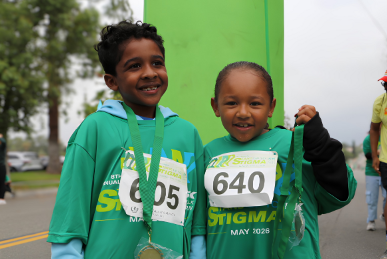 Two children in green event shirts display finisher medals at a 5K finish line.