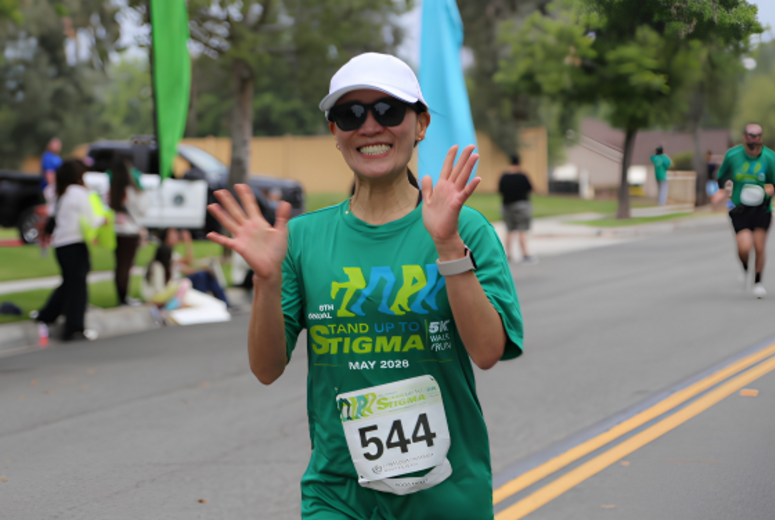 Participant in green event shirt waves while walking in a 5K; bib number 544.