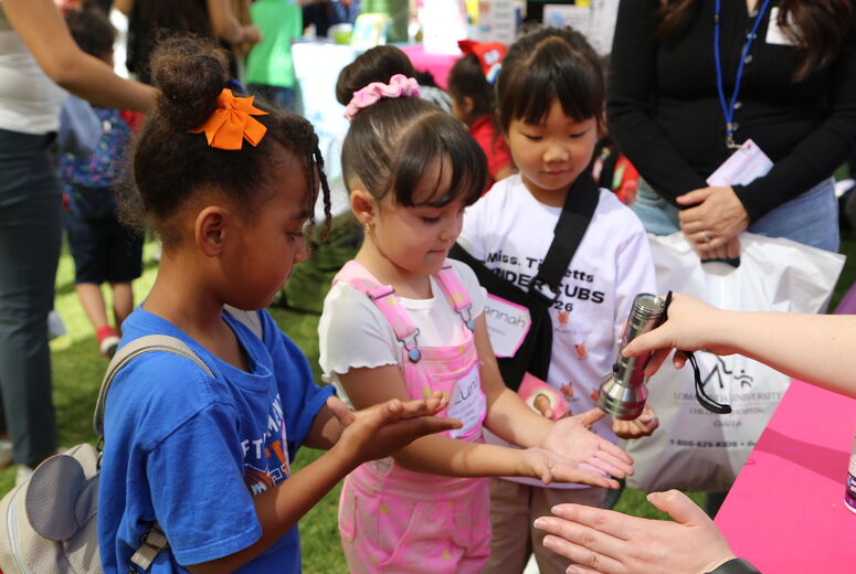Children look at their hands under a UV light held by an adult to check for leftover germs after washing.