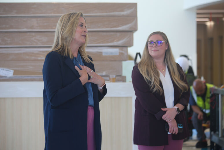 Woman speaks while another woman stands in background. Construction workers can be seen in the back