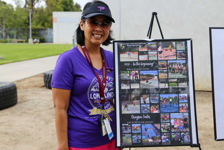 Kimberly Knowlton stands next to board of history of Loma Linda Pickleball club