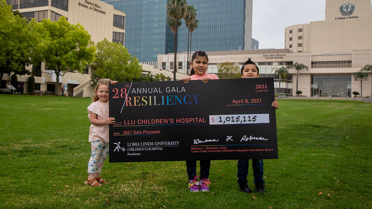 three kids standing in front of hospital with giant check