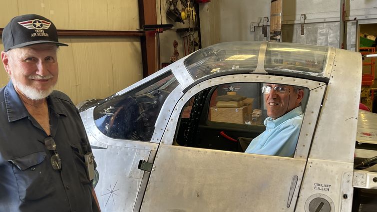 Joe Yancey shows Dr. Akhtari his hangar as Dr. Akhtari sits in a world war II plane cockpit