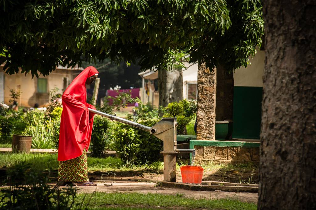 A Nigerian women dressed in red draws water from a local well.