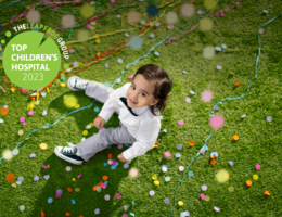 young boy with brown hair sitting in the grass, looking up with confetti falling.